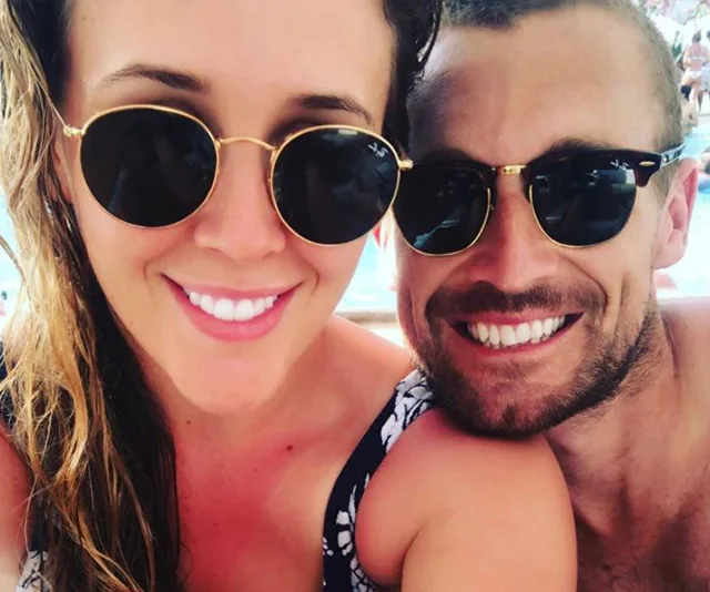 A couple smiling together wearing sunglasses, outdoors.
