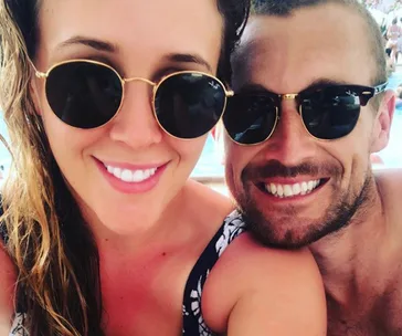 A couple smiling together wearing sunglasses, outdoors.