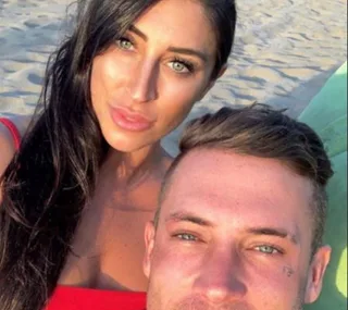Couple taking a selfie on a beach at sunset with sand in the background.