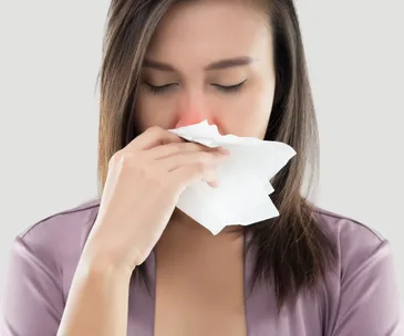 Woman with closed eyes holds tissue to nose, indicating cold or allergy.