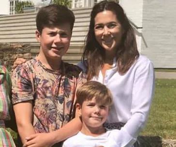 A woman and two boys pose outside on a sunny day, standing close and smiling.