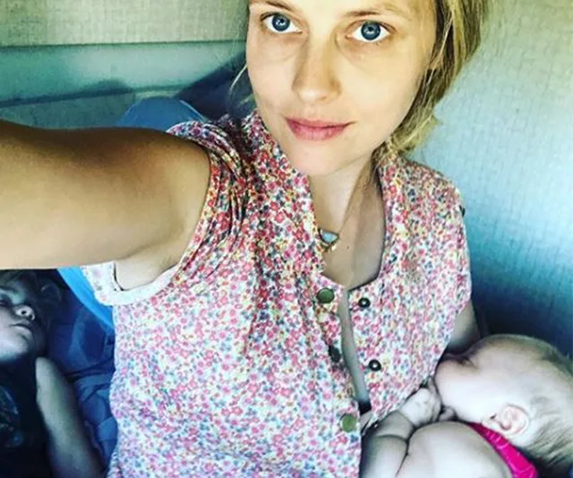 Woman in a floral top taking a selfie with a sleeping baby and child beside her.