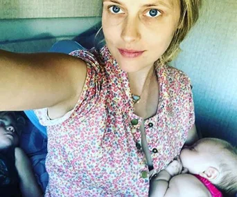 Woman in a floral top taking a selfie with a sleeping baby and child beside her.