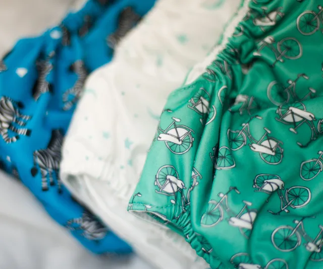 Colorful cloth diapers with bicycle and zebra patterns in green, white, and blue arranged side by side.