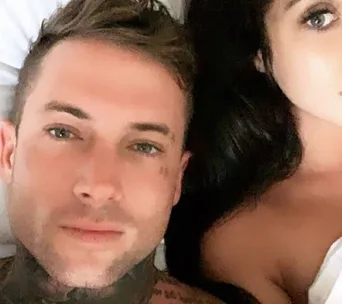Man with tattoos lying next to a woman in bed.