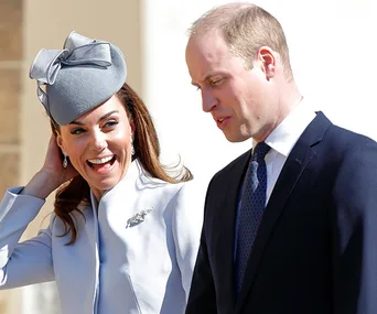 Two individuals in formal attire and hats, smiling outdoors.