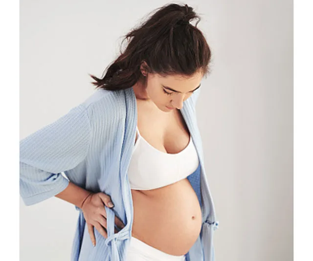 Pregnant woman looking at her belly, wearing a white bra and light blue robe.