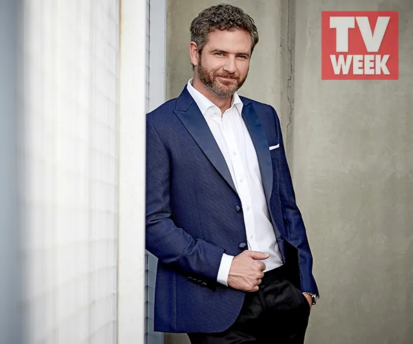 A person in a blue suit leans against a wall, featured in TV WEEK.
