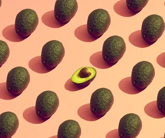 Pattern of whole avocados on a pink background with one cut in half, revealing the seed.