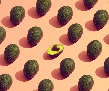 Pattern of whole avocados on a pink background with one cut in half, revealing the seed.