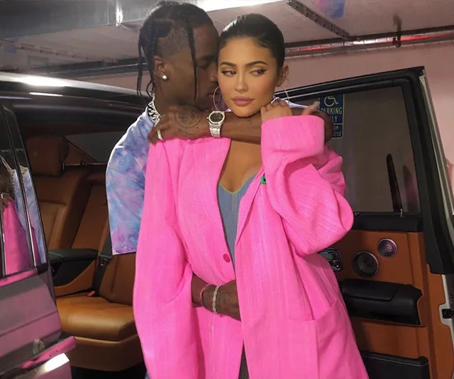 Two people in a parking garage, one in a pink outfit, standing beside a car.