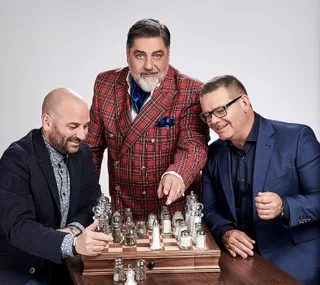 Three men in suits play with a chessboard of salt and pepper shakers, smiling and engaged.