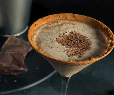 Creamy chocolate martini topped with chocolate shavings in a glass rimmed with cocoa powder.