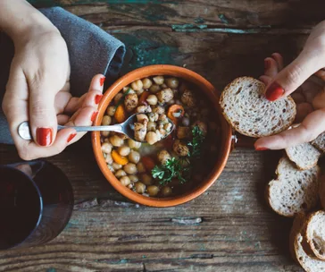 Person eating a Mediterranean chickpea stew with sliced bread on a wooden table.