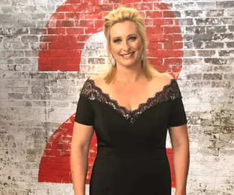 Woman in elegant black dress with lace detail standing in front of brick wall with red number 2.