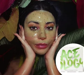 A person wearing a green speckled face mask surrounded by tropical leaves, with Acology face mask packaging shown.