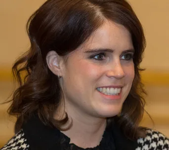 A woman with dark hair smiles warmly, wearing a black and white patterned outfit.