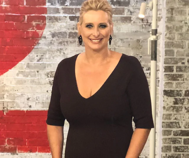 Person smiling in front of a textured wall with a painted red heart.