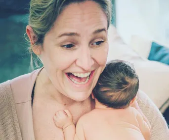 Smiling woman holding a baby on her shoulder in a cozy setting.