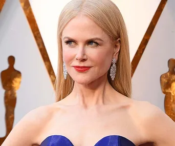 Nicole Kidman in a blue gown with diamond earrings at the Oscars, posing confidently.