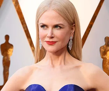 Nicole Kidman in a blue gown with diamond earrings at the Oscars, posing confidently.