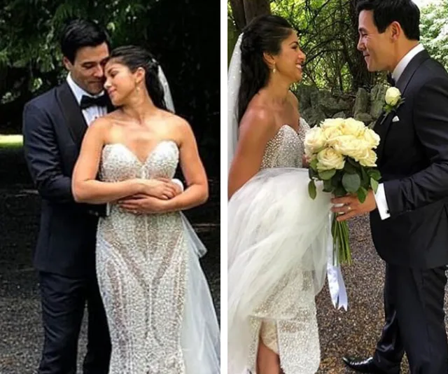 Bride and groom in elegant attire embracing and smiling outdoors, with bride holding a bouquet of white roses.