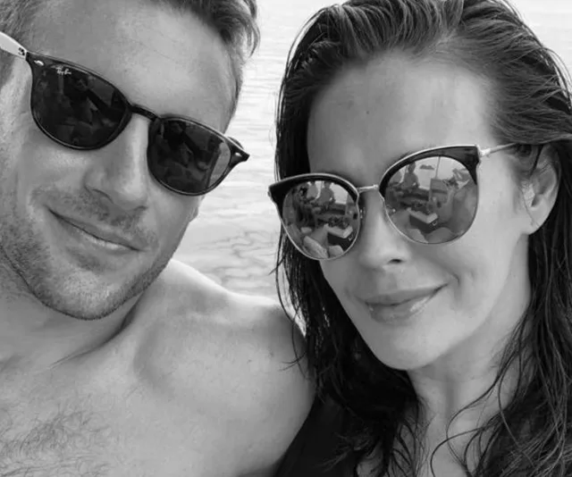 Two people wearing sunglasses smiling at the camera, reflecting a scenic outdoor view in black and white.