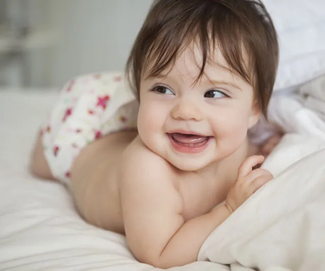 Smiling baby lying on bed wearing a floral disposable nappy.