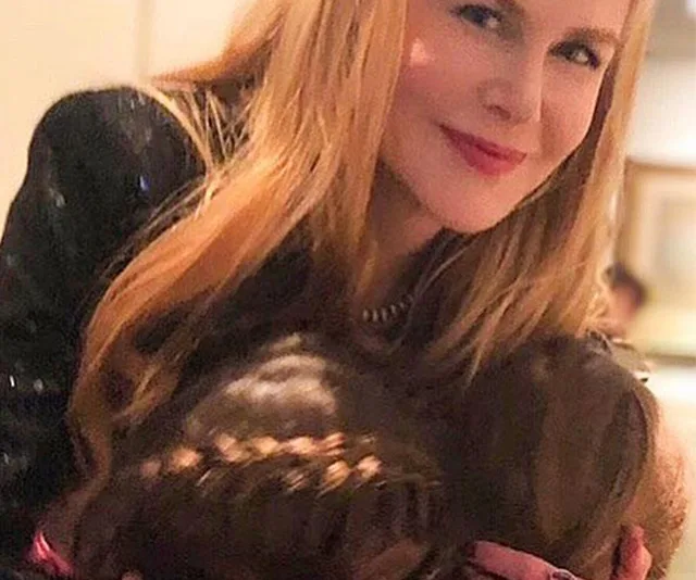A woman with long blonde hair smiles softly while embracing a child with brown braided hair.