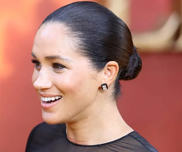 Meghan Markle smiling at an event, wearing a black dress and square earrings.