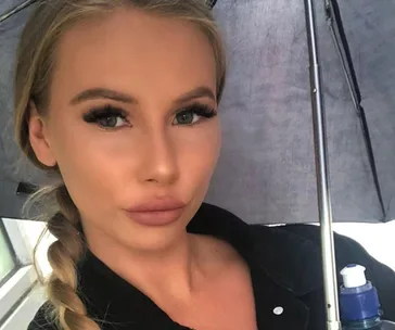 Young woman with braided hair under an umbrella, wearing a dark top, holding a water bottle.
