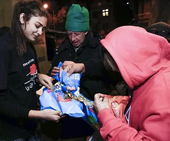 People distributing food to individuals in need at night, with bags of snacks being handed out.