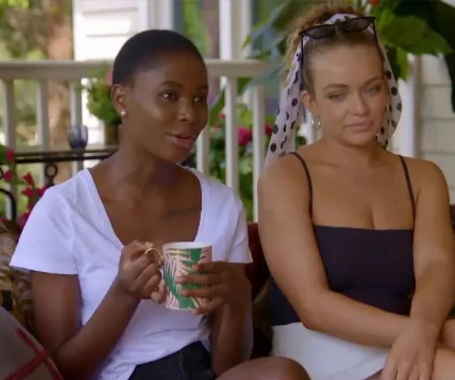 Women sitting on a porch, one in a white tee holding a mug, the other in a black top with a polka dot headband.