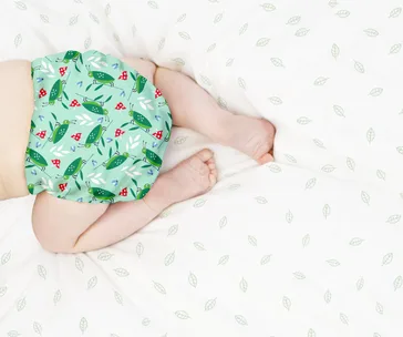 Baby wearing a green, patterned cloth nappy on a bed with leaf-print sheets.