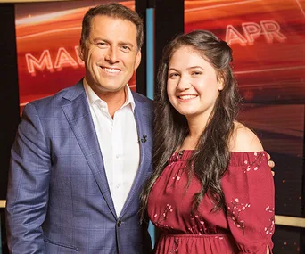 Karl Stefanovic smiling with a woman in a red dress on a TV show set.