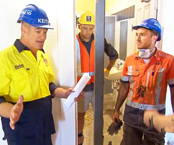 Construction workers Keith and Jesse discuss plans in a partially completed building interior.