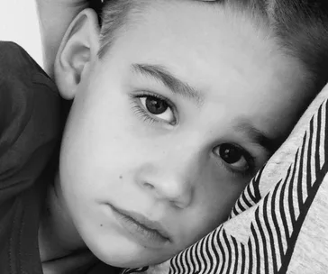 Young boy resting his head with a sad expression, close-up black and white photo.