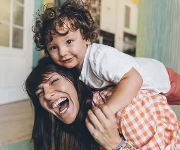 Mom smiling with child on her back at home, both happy.