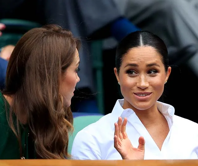 Two women seated at an event, engaged in conversation, one gesturing with her hand.