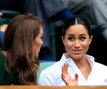 Two women seated at an event, engaged in conversation, one gesturing with her hand.