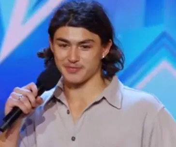 Young man with long hair holding a microphone on a colorful stage background.