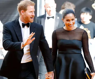 Two people in formal wear, smiling and holding hands at an event.
