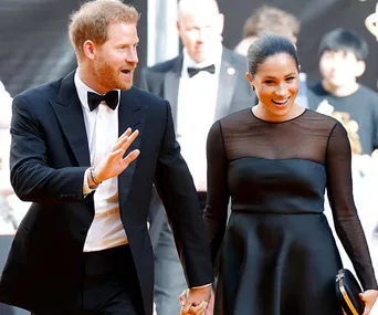 Two people in formal wear, smiling and holding hands at an event.
