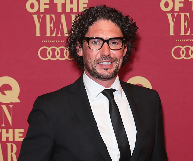 Colin Fassnidge in a suit at a red carpet event with "GQ Men of the Year" backdrop.