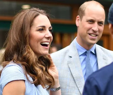 A woman and man smiling while conversing outdoors, both dressed in formal attire.