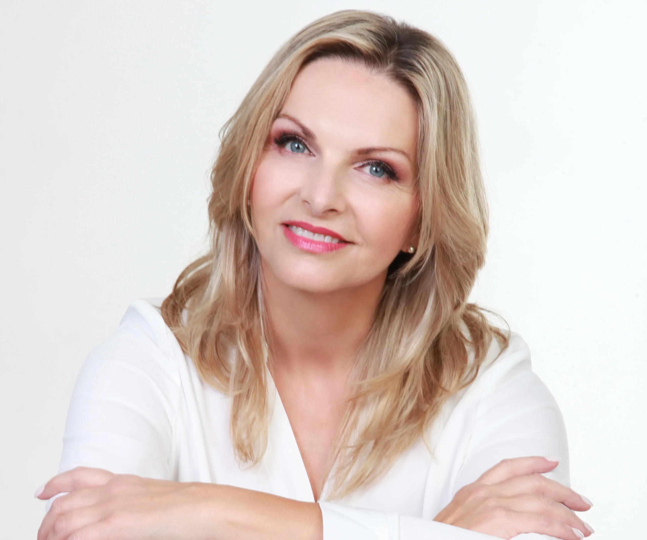 A smiling woman with blonde hair and a white top, against a plain background.