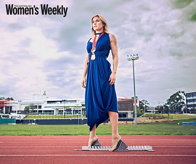 Athlete wearing a blue dress and medals, standing on a running track.