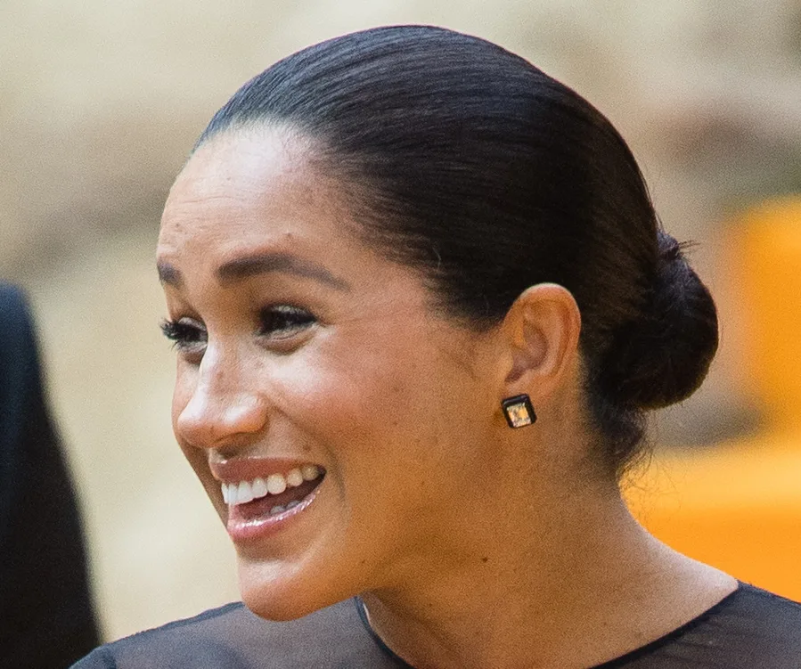 Smiling person with dark hair in a bun, wearing square earrings.