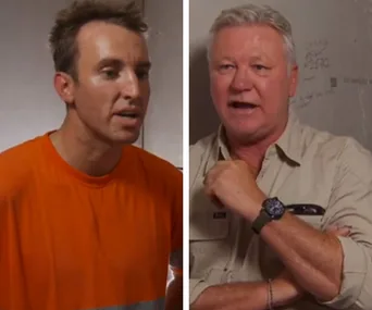 Two men in a tense conversation, one in an orange shirt and the other in a light-colored shirt, against a plain background.