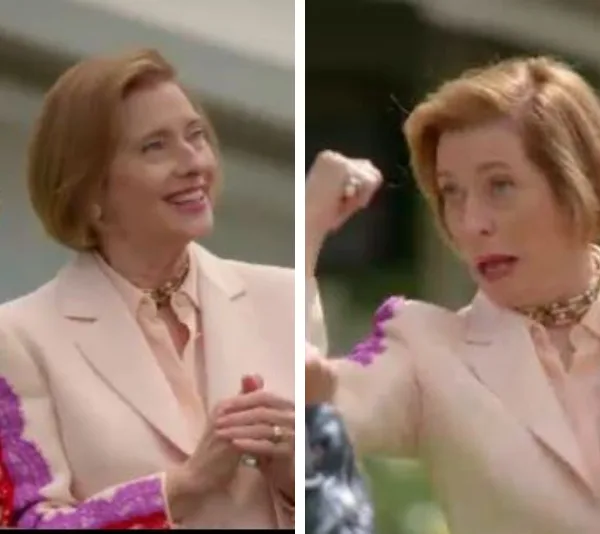 "Blonde woman in a pale suit making animated gestures outdoors."